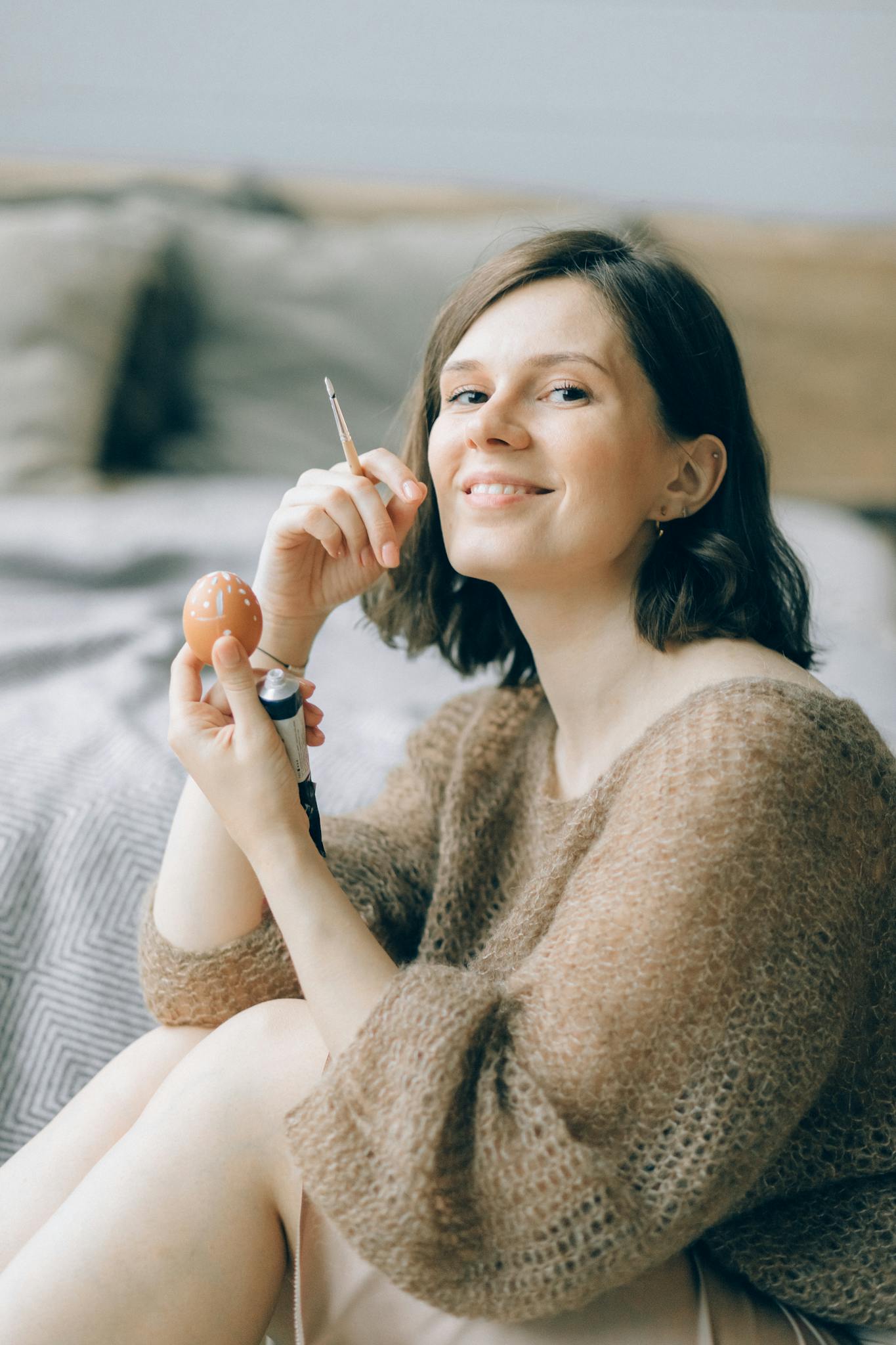 Adult woman joyfully painting an Easter egg indoors. Spring seasonal activity with a handmade touch.