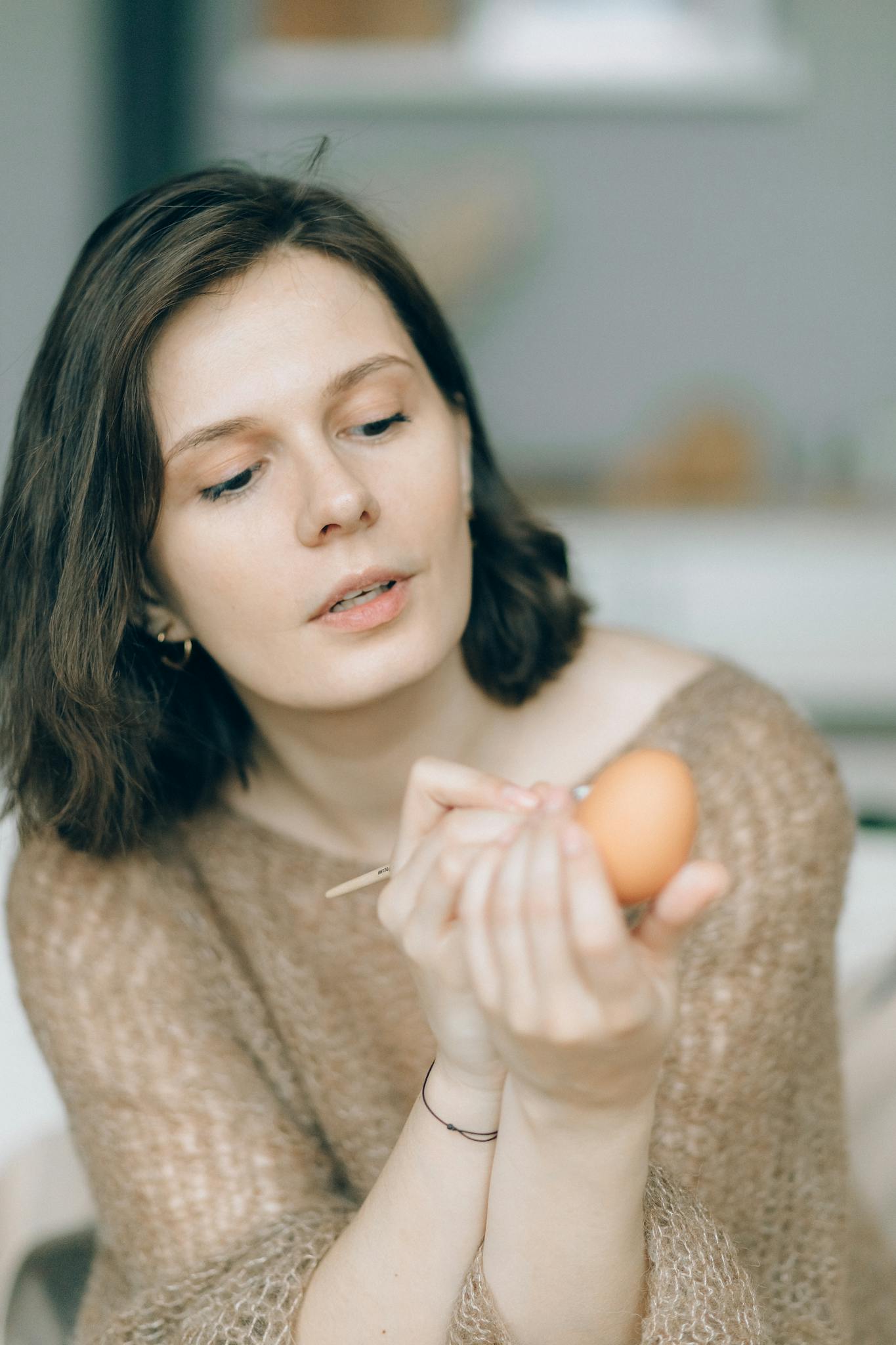 A woman carefully painting an Easter egg in a cozy indoor setting, embracing a festive and creative moment.