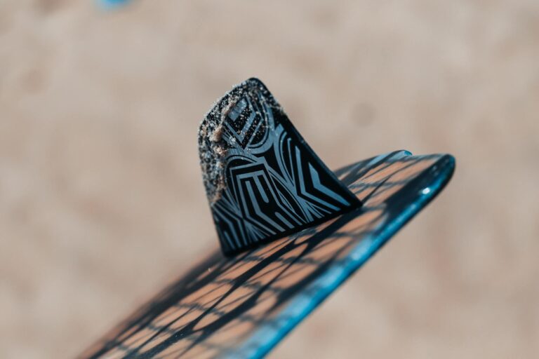 Detailed view of a surfboard fin with sand particles against a blurred beach background.